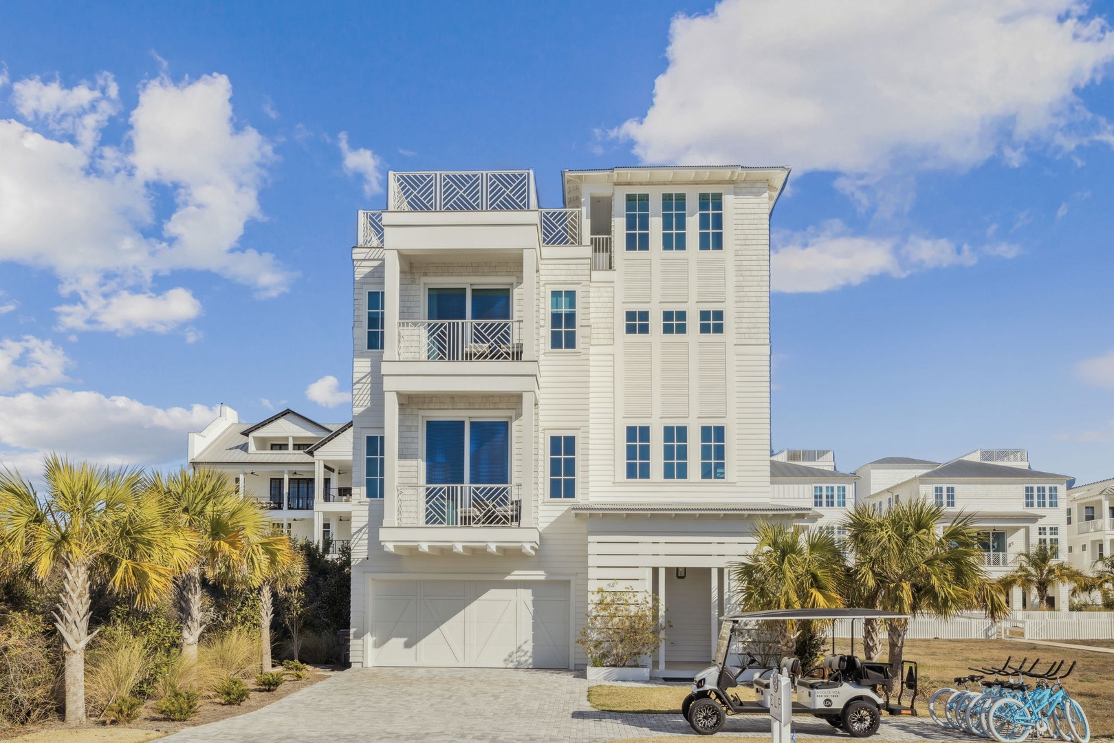 Modern three-story beach house with elegant white siding and decorative railings in a coastal neighborhood setting.