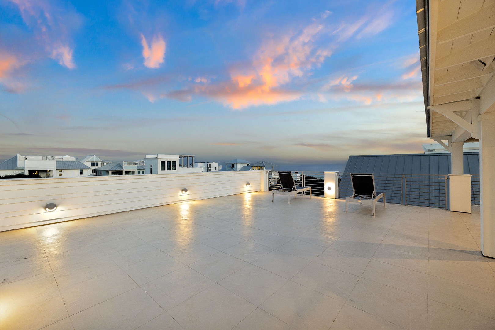 Stunning rooftop terrace captures golden sunset hues over contemporary coastal homes, creating the perfect backdrop for your evening relaxation.