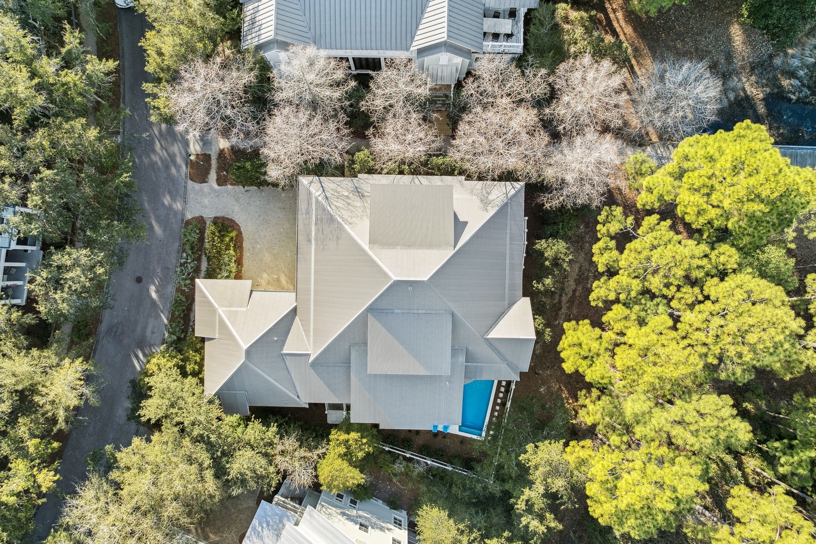 Aerial view showcasing the property's contemporary architecture nestled among mature trees in a quiet residential neighborhood with swimming pool.