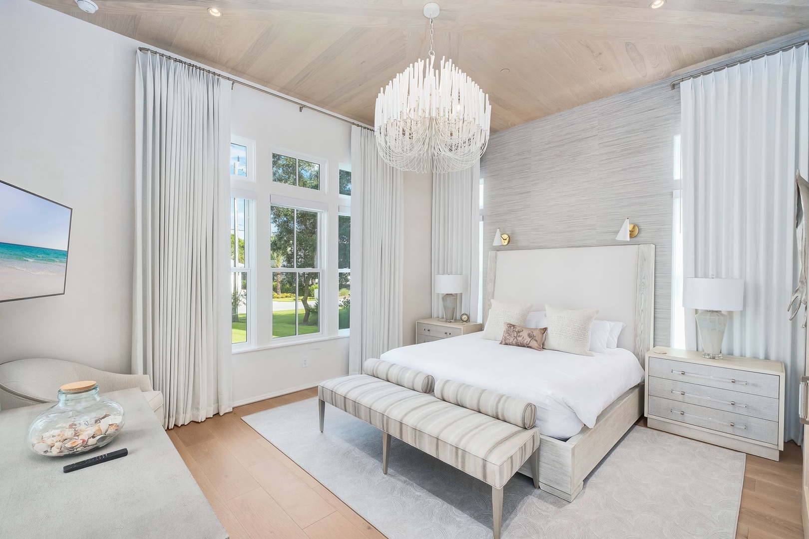 Drift into peaceful dreams in your elegant primary suite, where soft textures and soaring ceilings create a tranquil sanctuary beneath a stunning chandelier.