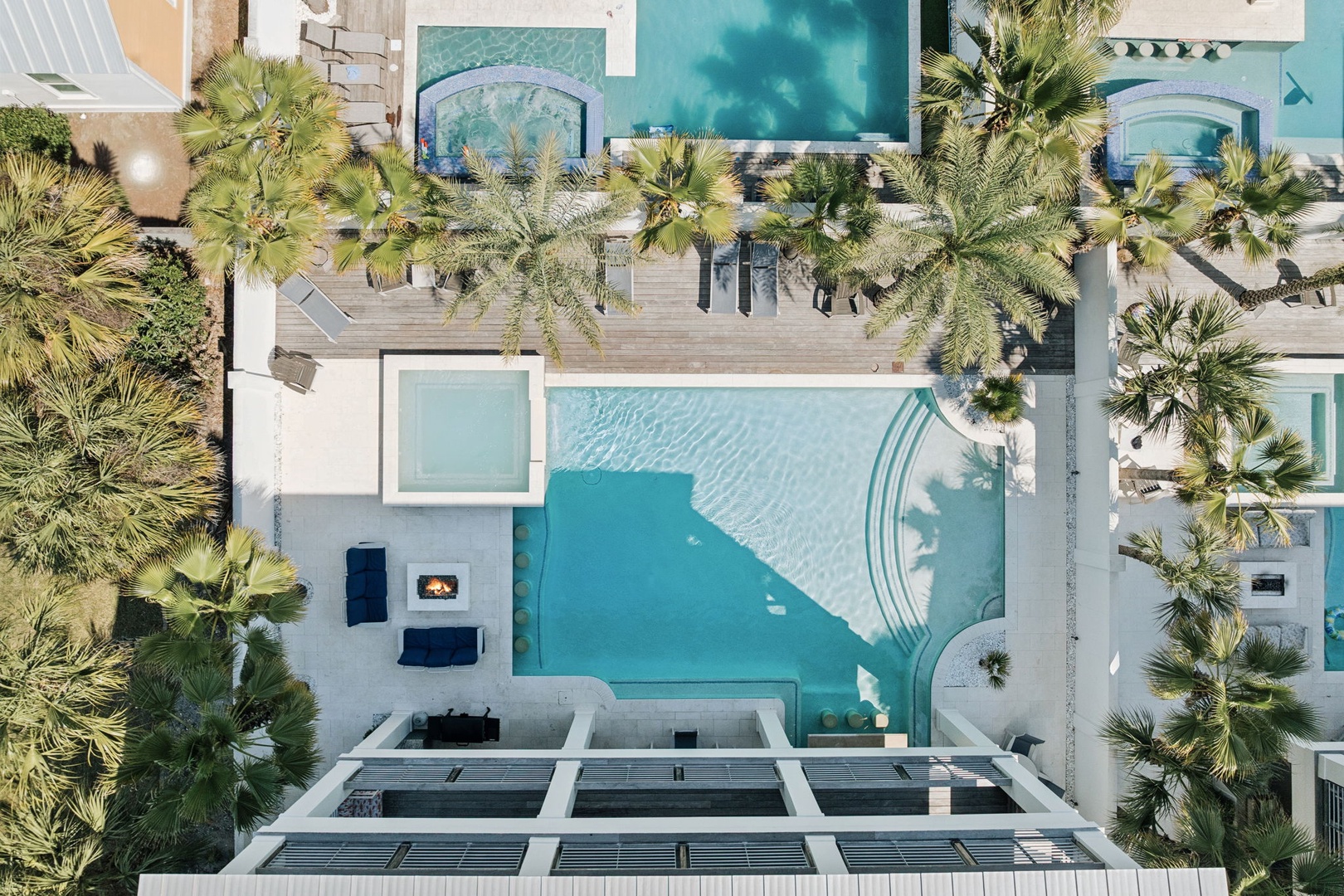 Aerial view of luxury villa complex with stunning swimming pools surrounded by tropical palm trees and modern architecture.