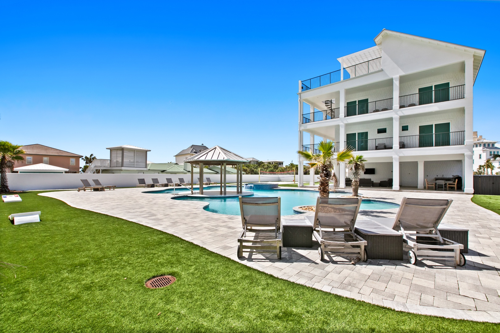 This modern beachside property features a sparkling resort-style pool with a unique circular swim-up bar, expansive sun deck with lounge chairs, and multiple private balconies overlooking lush landscaping.