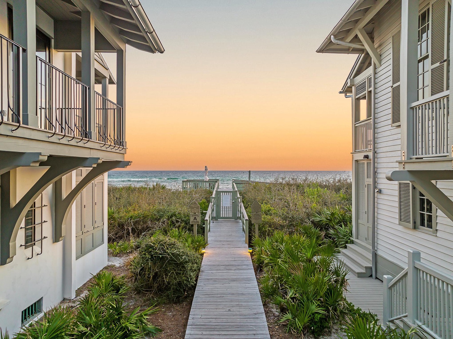 Beachfront property buildings frame a wooden boardwalk leading directly to pristine ocean shores during golden hour.