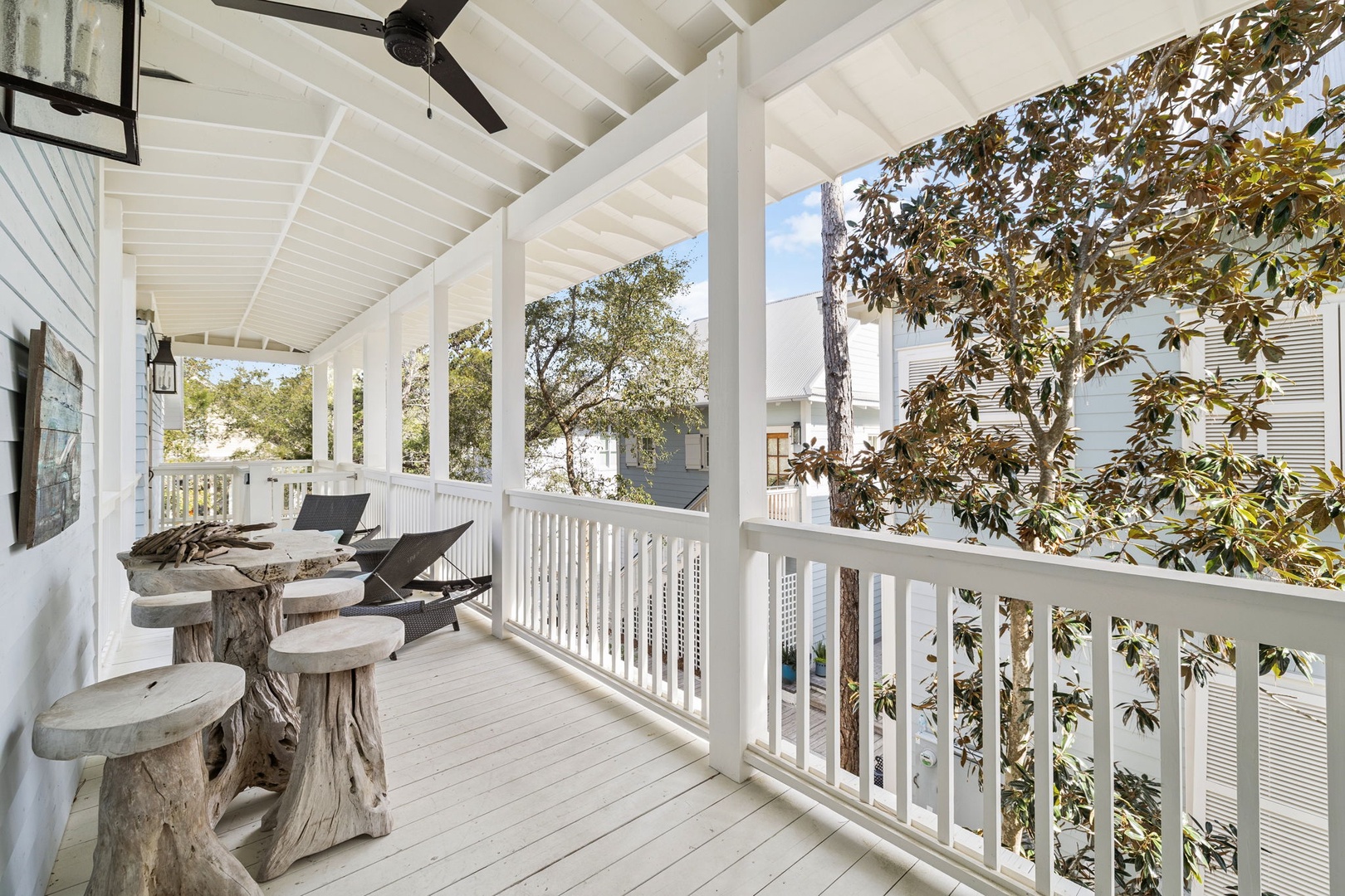 Unwind on your private covered balcony with rustic seating and cooling ceiling fan, surrounded by lush greenery.