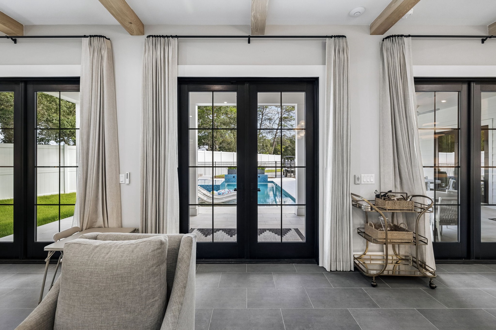 Step into a bright, airy living space where soaring ceilings with exposed wood beams frame stunning glass doors that open to your private pool oasis. Natural light floods through every window, creating a seamless indoor-outdoor retreat.