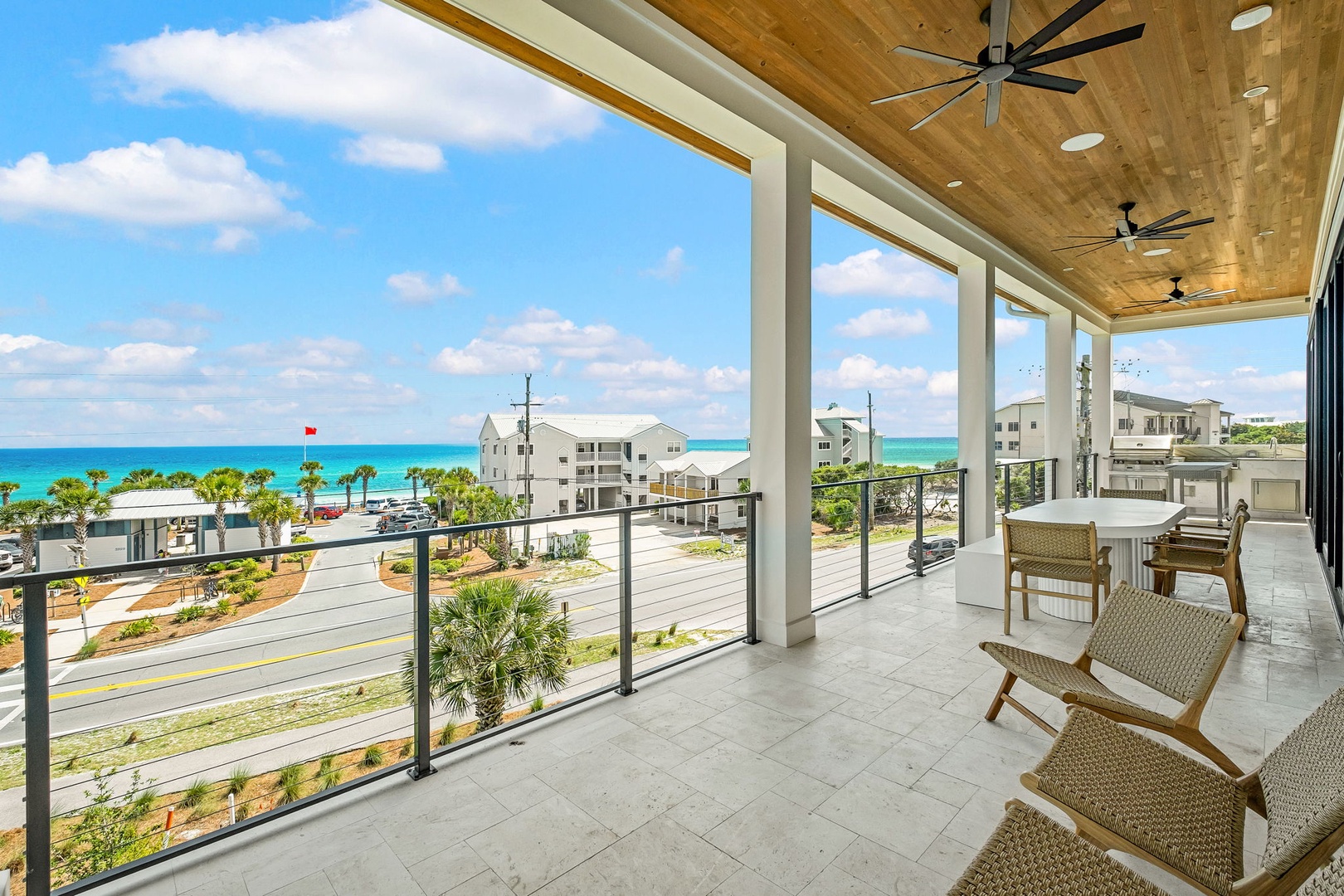 Picture yourself unwinding on this expansive covered terrace, where stunning sea views and warm coastal breezes create your perfect retreat. Relax in stylish seating beneath a wood-paneled ceiling with cooling fans.