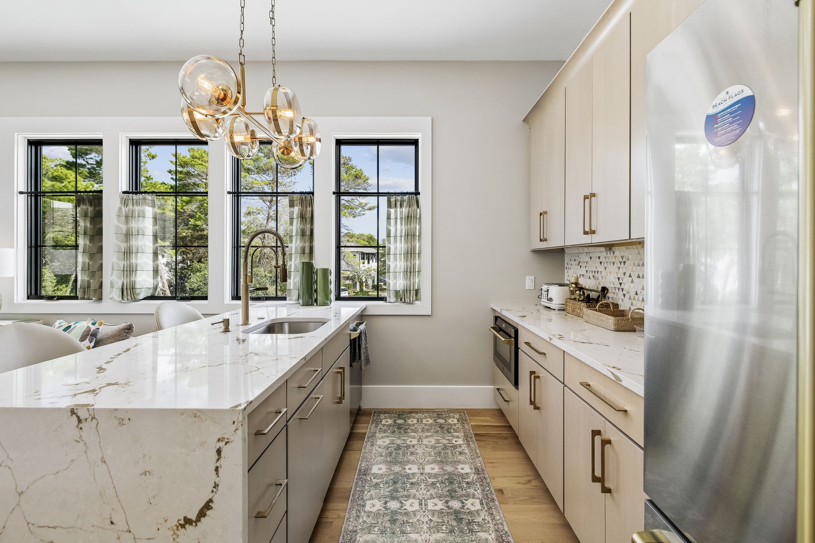 Prepare your favorite meals in this bright, modern kitchen with elegant marble countertops and stainless appliances. Sunlight pours through large windows overlooking lush greenery, making your cooking experience feel relaxed and inspired.