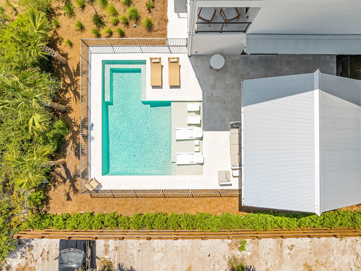 Aerial view of the modern rental property featuring a pristine private pool surrounded by sunloungers and lush landscaping, with the main building and outdoor terrace visible.