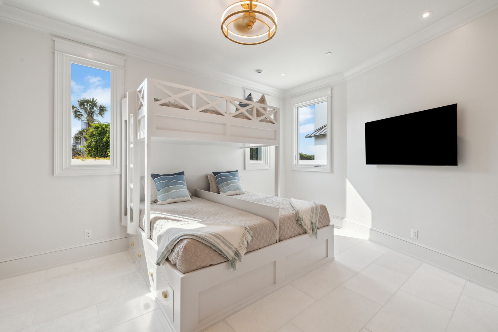 Bright, airy bedroom with a charming bunk bed setup perfect for families. Natural light pours in through multiple windows, while the wall-mounted TV adds modern convenience to your coastal retreat.