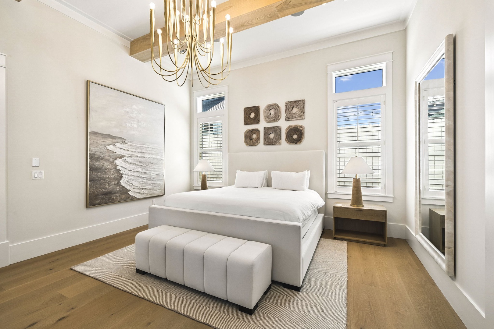 Sink into plush bedding beneath soaring ceilings and elegant wood beams, where natural light floods through plantation shutters and coastal-inspired art sets a serene, restful tone.