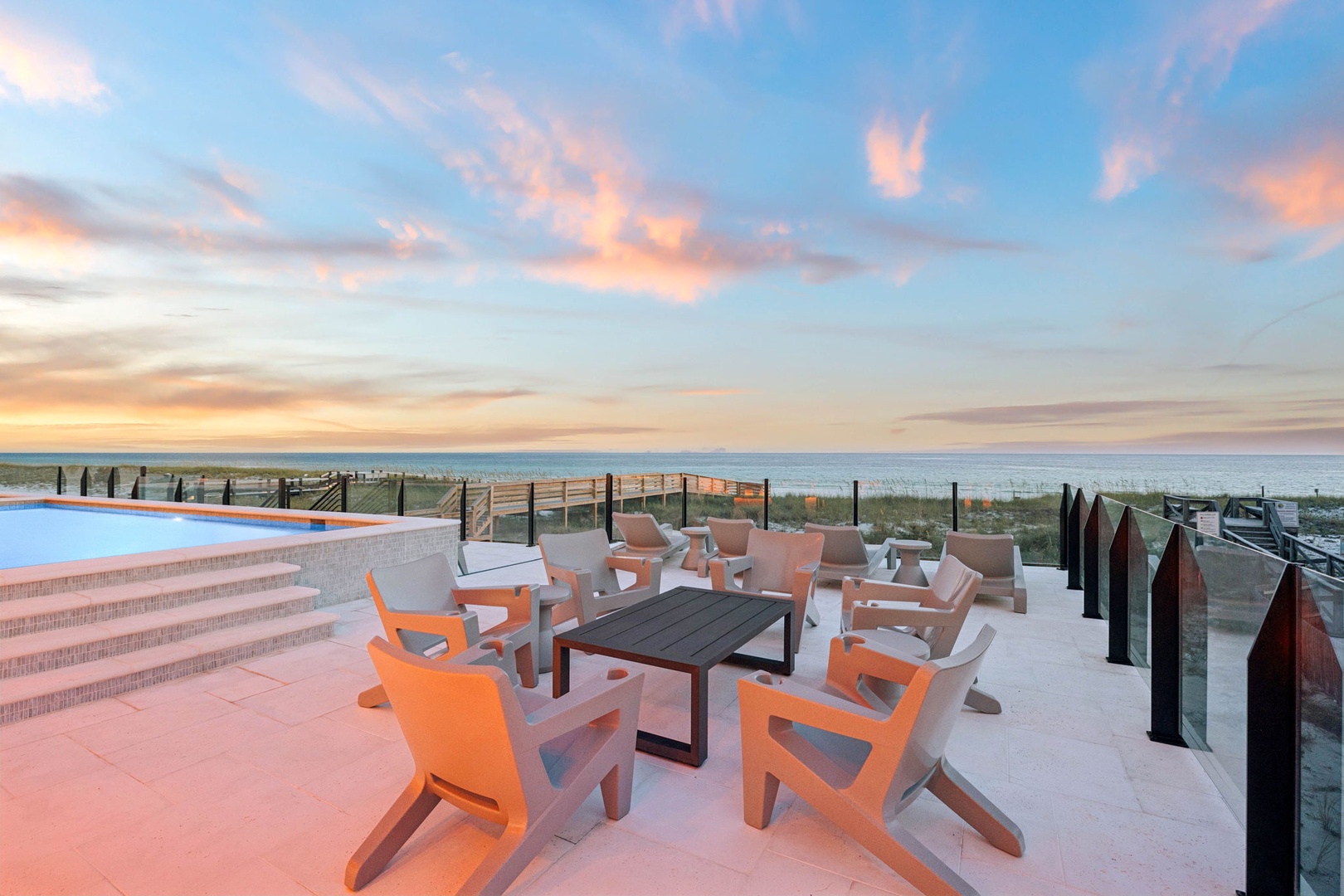 Beachfront terrace features stylish lounge seating and ocean views, with pool steps leading to a stunning infinity edge overlooking the shore.