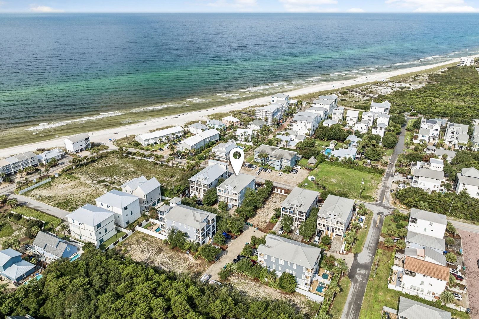 This beachfront property sits steps from white sand and emerald waters in a peaceful coastal neighborhood, with natural dunes and greenery defining the surrounding landscape.