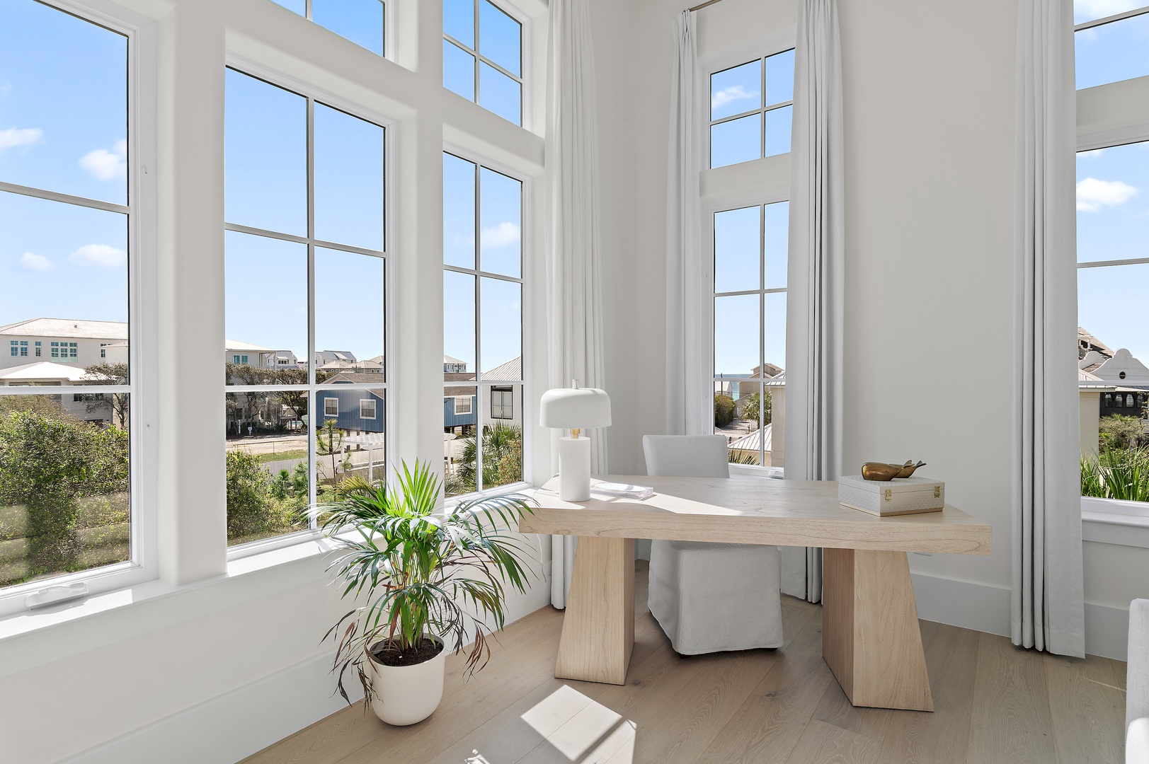 Sunlight pours through tall windows into your airy workspace, where a sleek desk and modern chair await. Fresh greenery and minimalist touches create a calm, inspiring retreat for catching up on work or enjoying morning coffee.