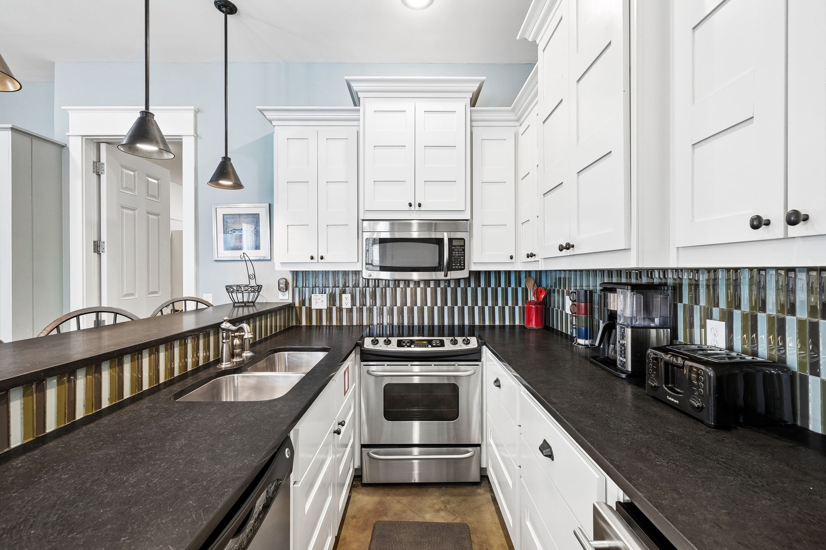 Step into your fully equipped kitchen where crisp white cabinetry meets sleek dark countertops. With stainless steel appliances and a colorful tile backsplash, you'll find everything you need to prepare delicious meals during your stay.