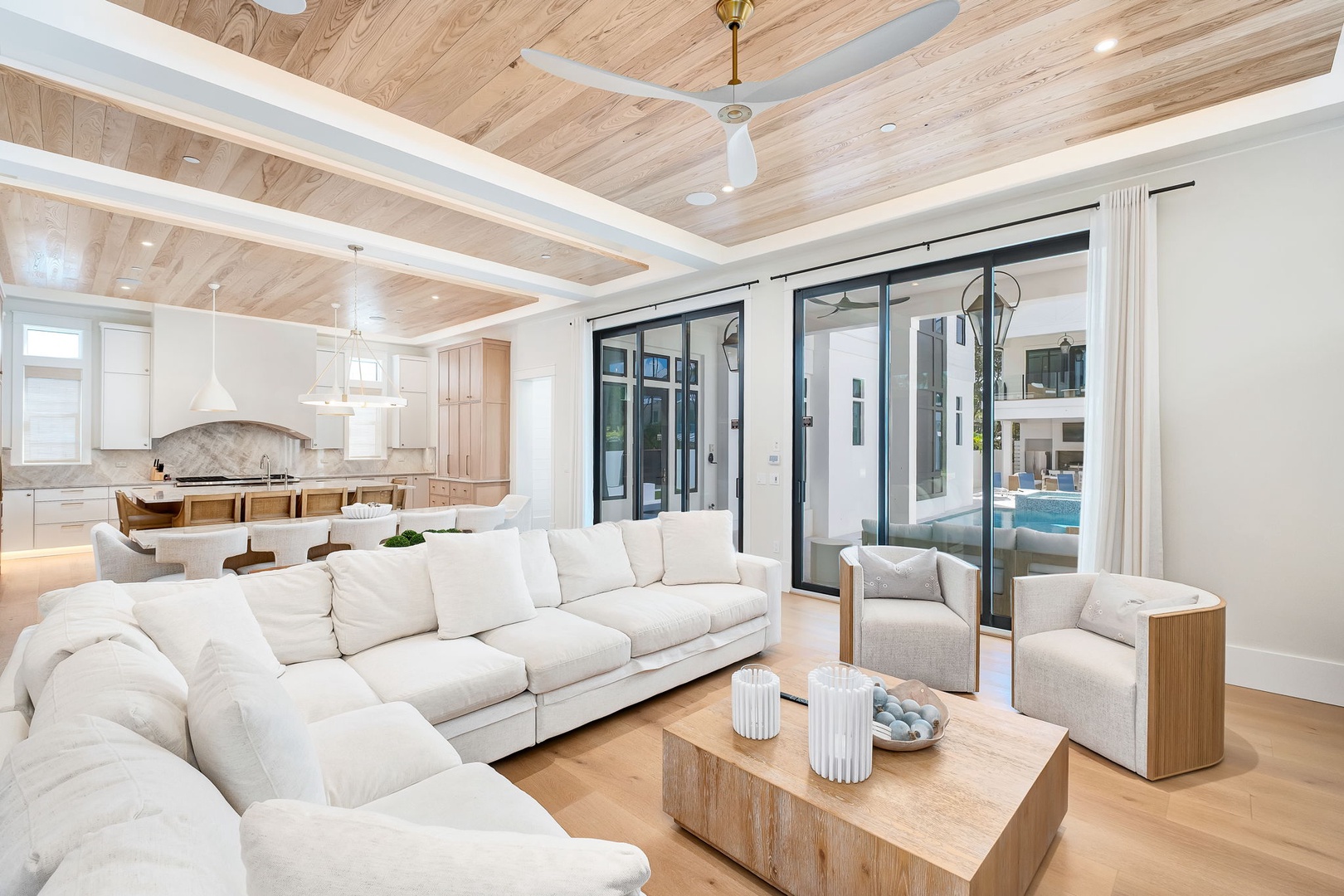 Sink into plush seating under beautiful wood-beamed ceilings while sunlight streams through floor-to-ceiling glass doors revealing your private pool beyond.