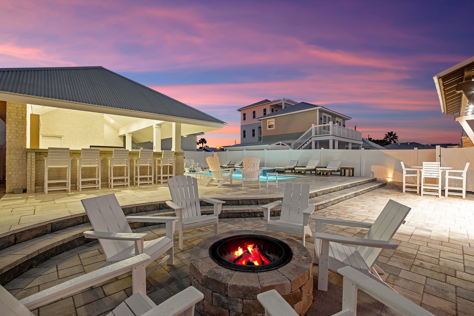 Stunning sunset skies paint the perfect backdrop for this elegant outdoor entertainment area with fire pit and pool.