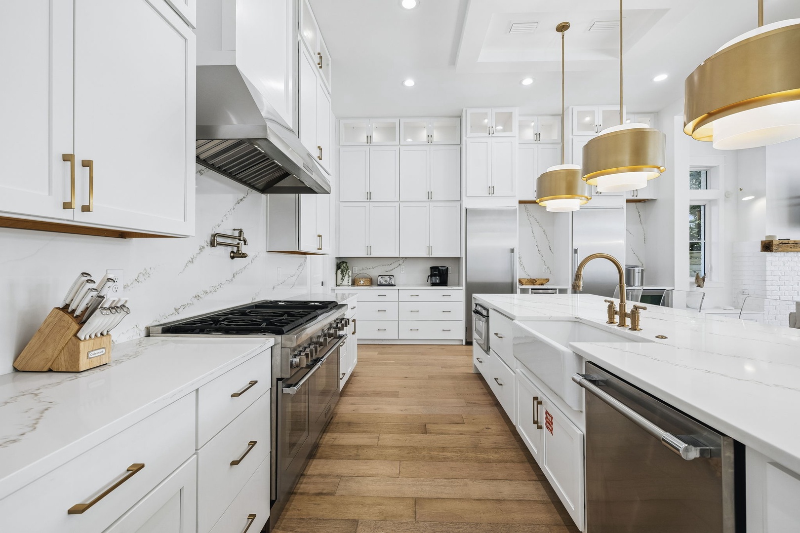 Step into a chef's dream kitchen: gleaming white cabinetry, marble countertops, and elegant brass fixtures throughout. Your culinary adventures await in this bright, spacious cooking space.