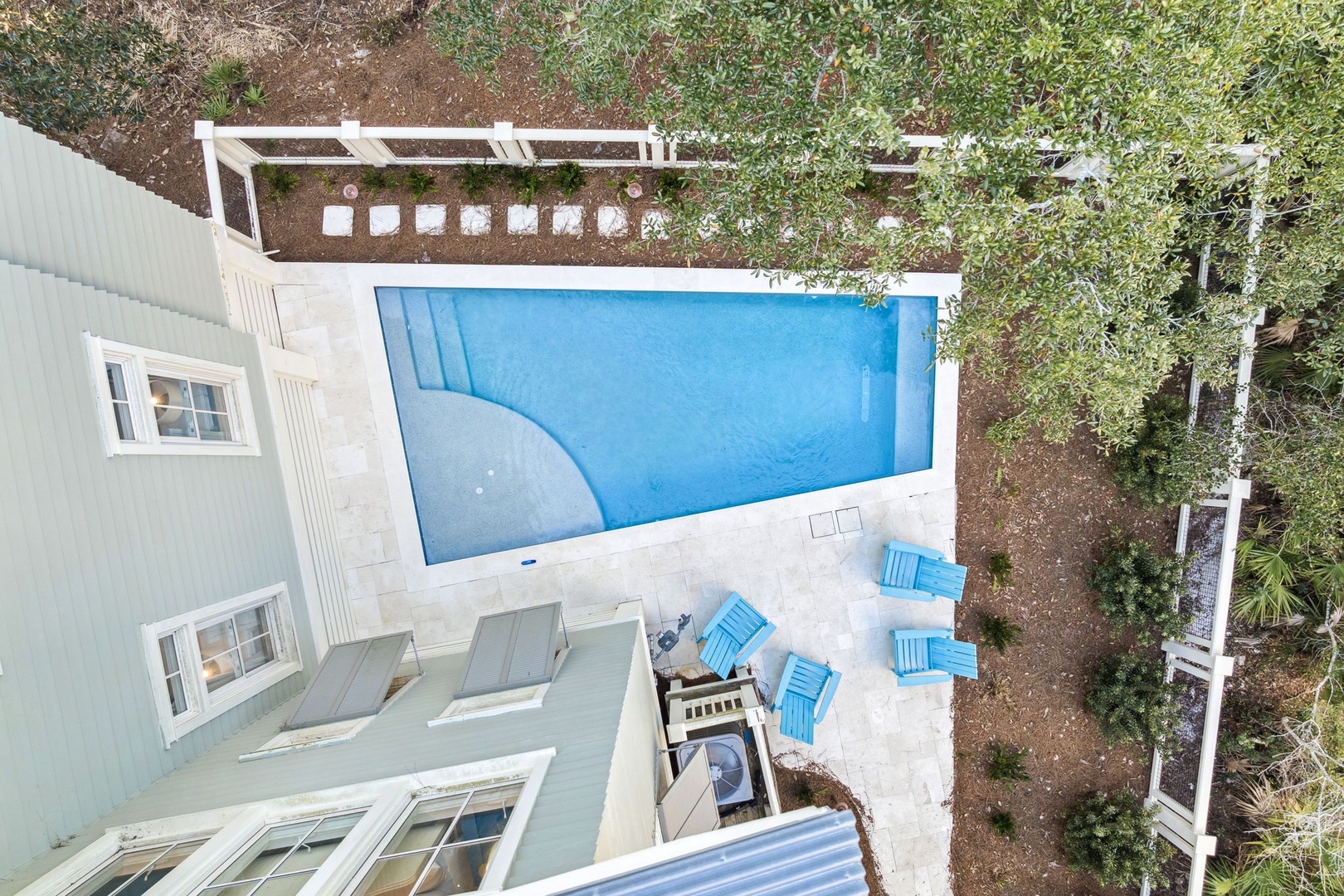 Aerial view of the property showing a sparkling blue swimming pool surrounded by a spacious patio and lush landscaping.