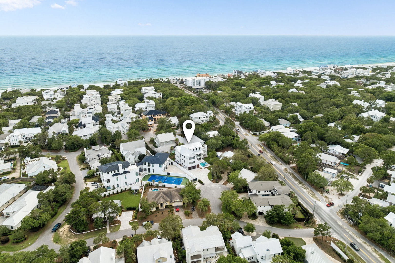 Aerial view showcasing a pristine coastal neighborhood just steps from emerald Gulf waters, with lush greenery surrounding vacation homes and the property marked at center.