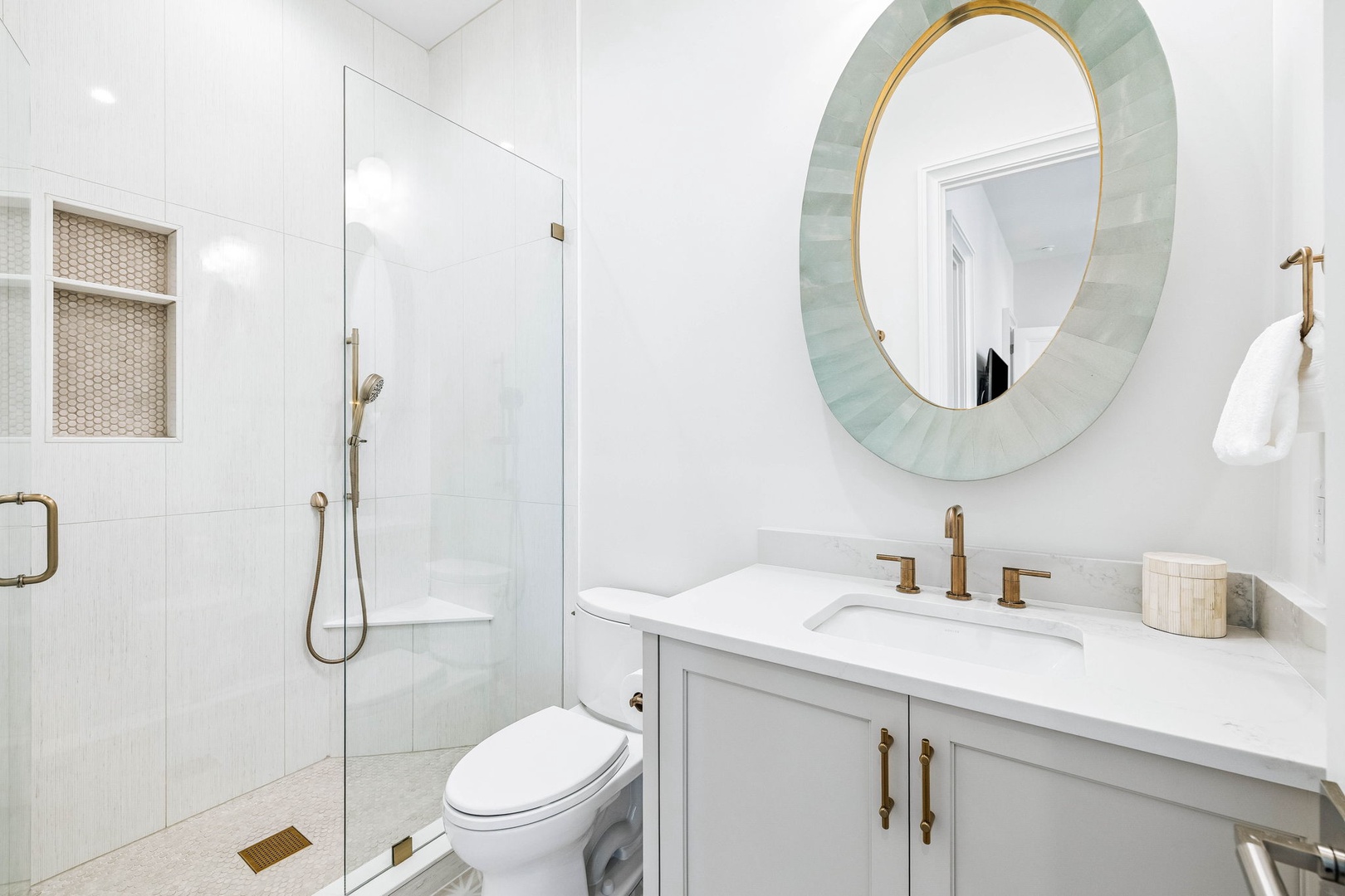 Step into your private spa-like retreat with gleaming white tile, a glass-enclosed shower, and elegant gold fixtures. The stunning seafoam mirror and pristine marble vanity create a serene sanctuary where you can unwind in style.