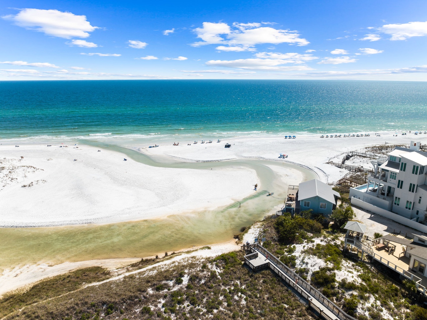 Stunning aerial view showcases pristine white sand beach meeting turquoise waters, with beachfront properties nestled among coastal dunes.