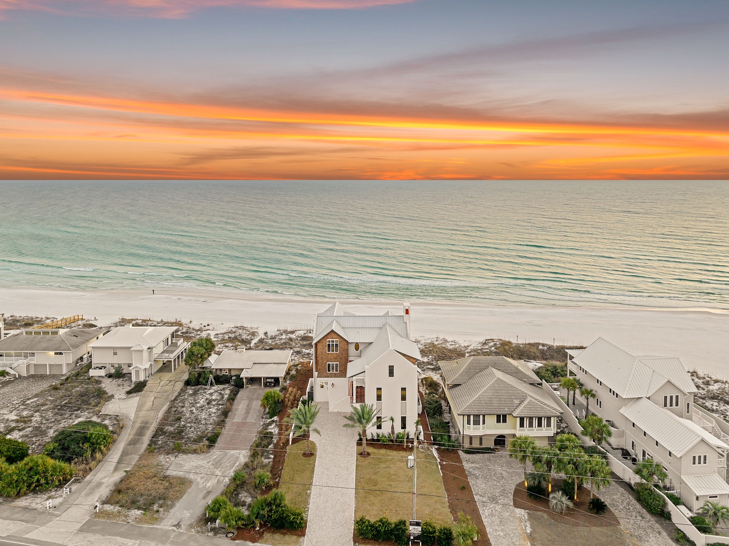 Stunning beachfront community showcases coastal architecture along pristine white sand shores beneath a dramatic sunset sky.