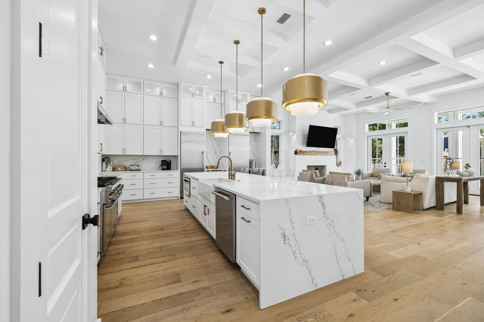 Step into your dream kitchen, where a stunning waterfall island awaits beneath elegant brass pendants. Gleaming white cabinetry and warm wood floors flow seamlessly into the inviting living space beyond, creating your perfect home away from home.