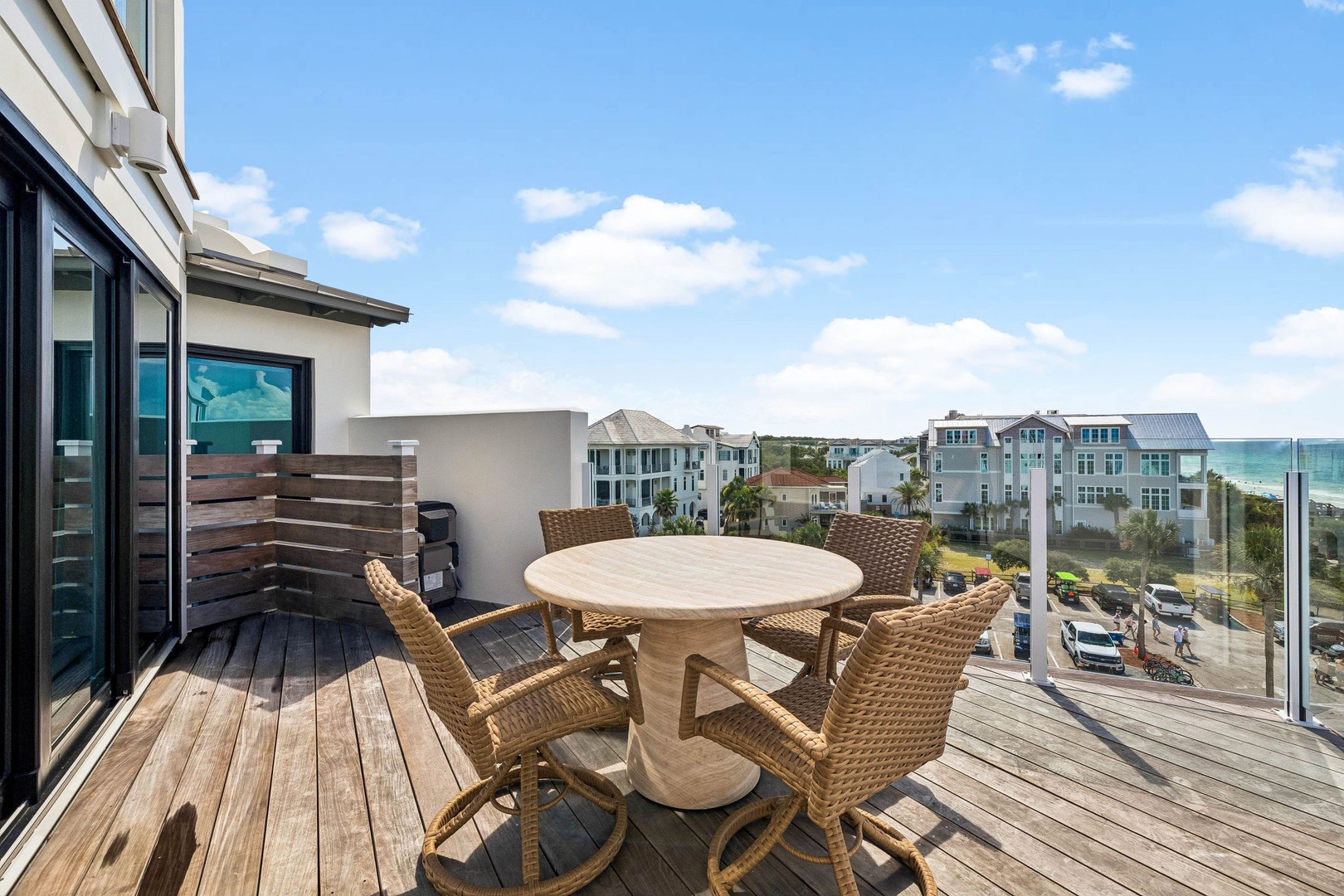 Rooftop deck with coastal neighborhood views and Gulf glimpses, featuring outdoor dining space with wicker seating and privacy screening—an elevated outdoor retreat near the shore.