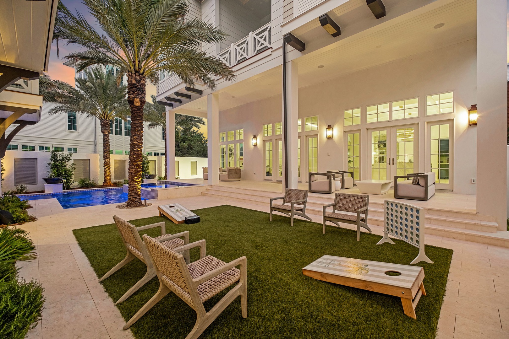 Your private courtyard invites you to unwind beneath swaying palms, with a sparkling pool nearby and game tables set for evening fun. Step inside through elegant French doors to discover a warm, welcoming retreat.