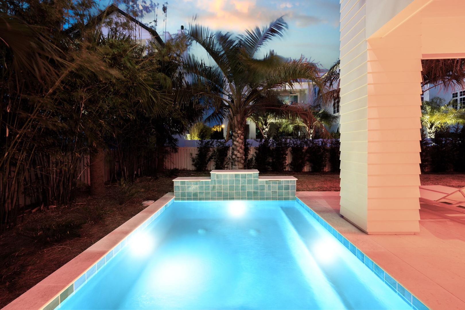 Your private pool glows invitingly as twilight settles, surrounded by lush palms and elegant columns for perfect evening relaxation.