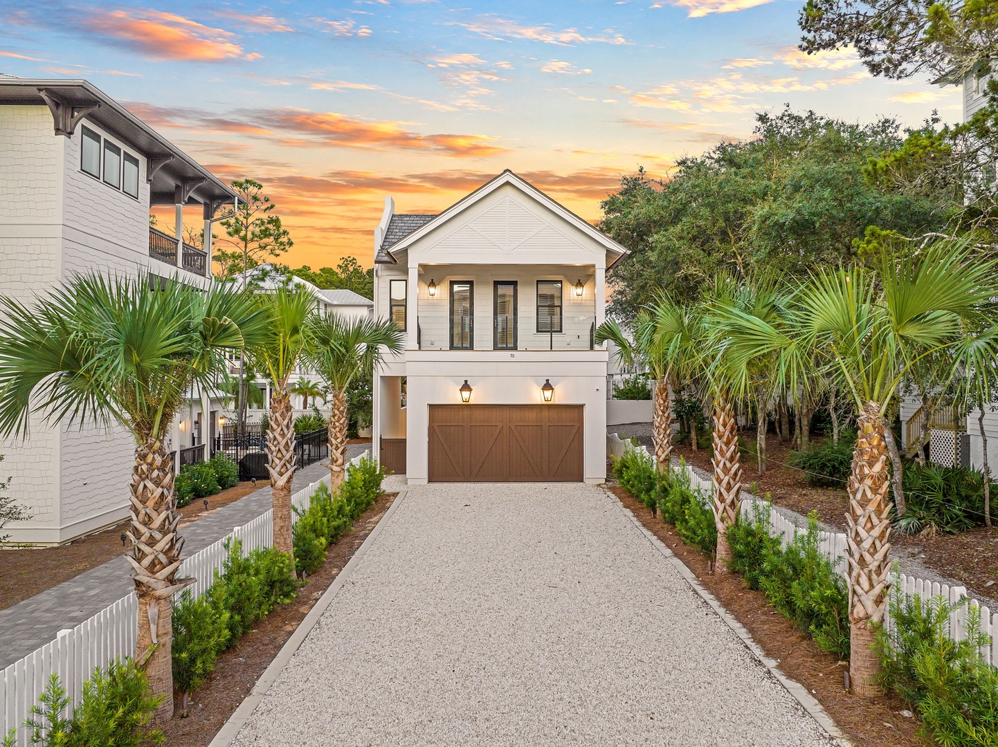 A charming coastal property framed by tropical palms with a modern farmhouse-style façade. The home sits in a tranquil neighborhood surrounded by lush greenery, welcoming guests at golden hour.