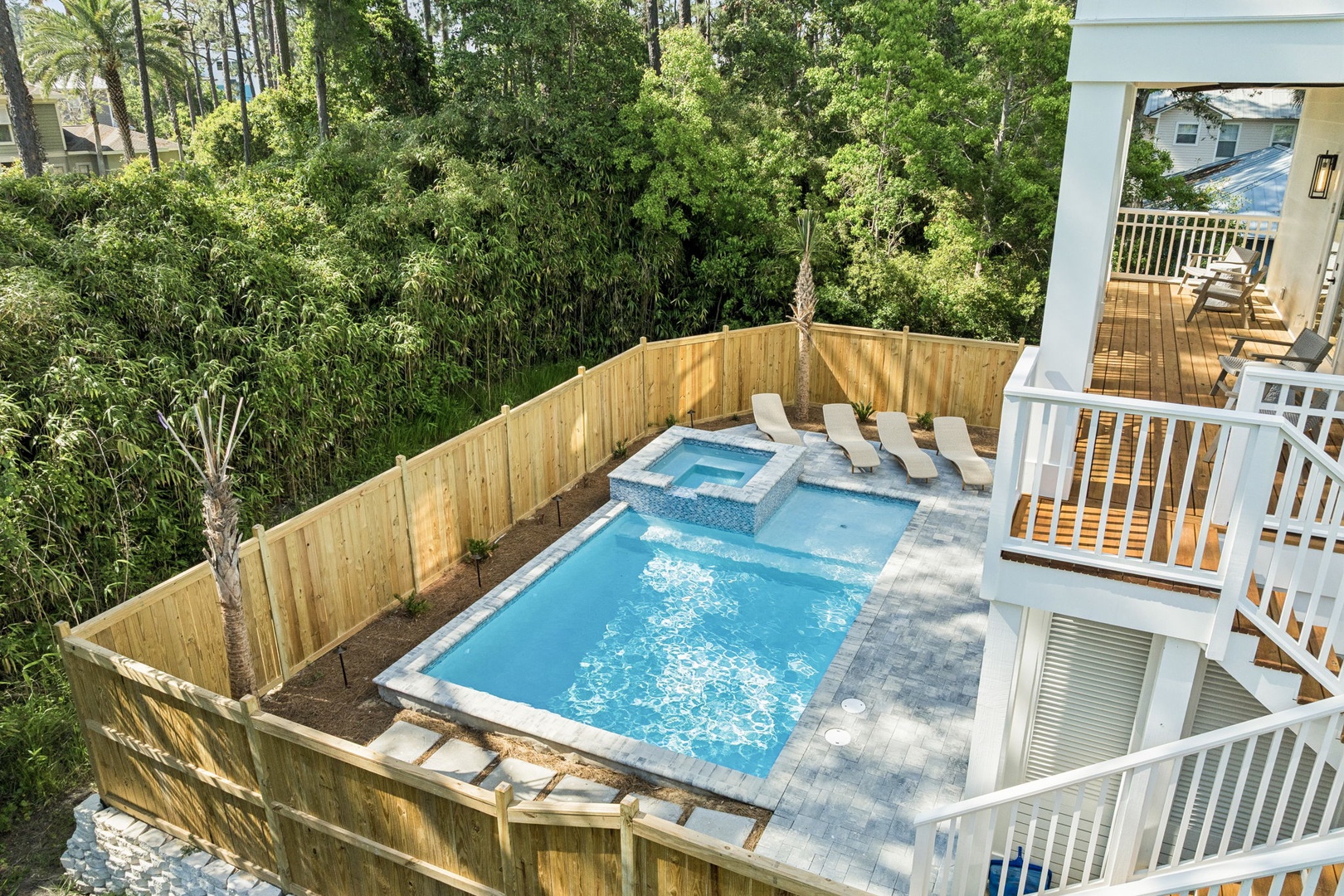 This property features a private swimming pool with an adjacent hot tub, surrounded by a spacious wooden deck with lounge seating and lush greenery creating a secluded backyard retreat.