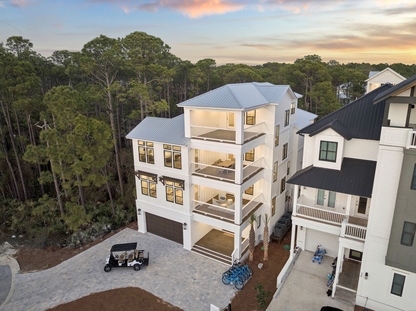 Modern multi-story vacation rental with expansive balconies and coastal architecture, surrounded by lush forest canopy at golden hour.