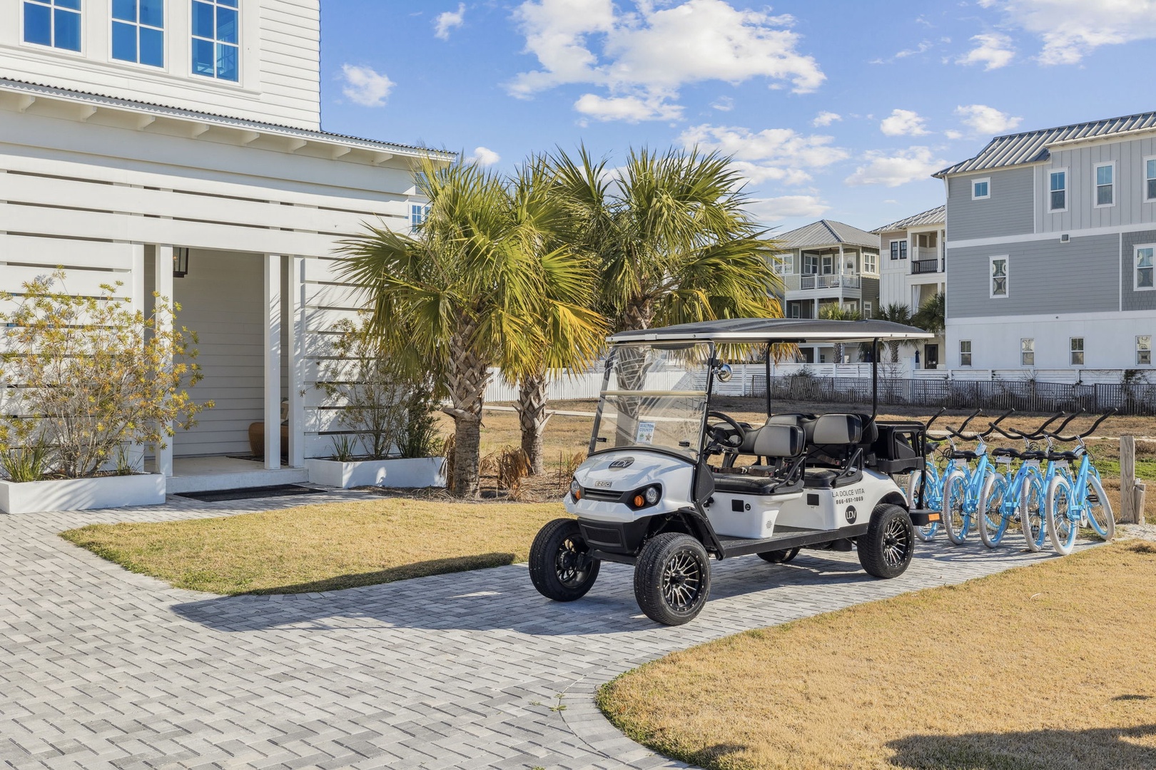 A beautifully landscaped property area featuring a golf cart and bicycle rack amid palm trees and coastal architecture.