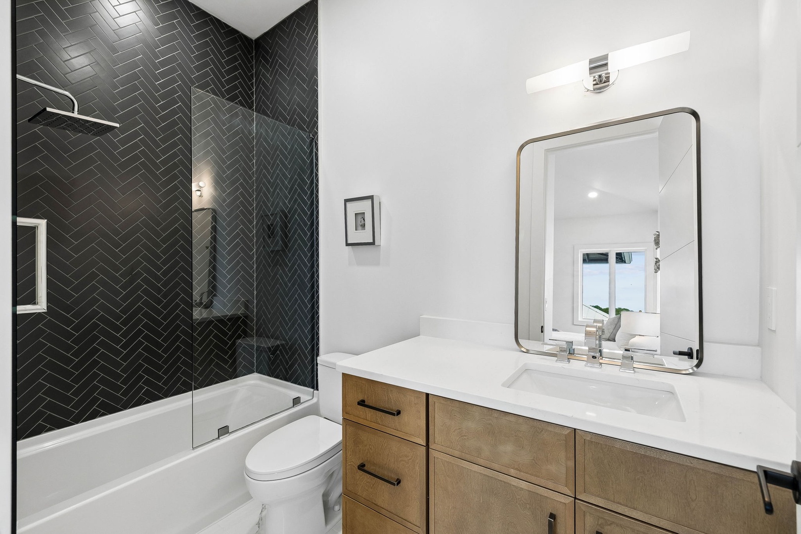 Step into your sleek modern bathroom with striking herringbone tile, warm wood vanity, and crisp white counters—designed for comfort and style during your stay.