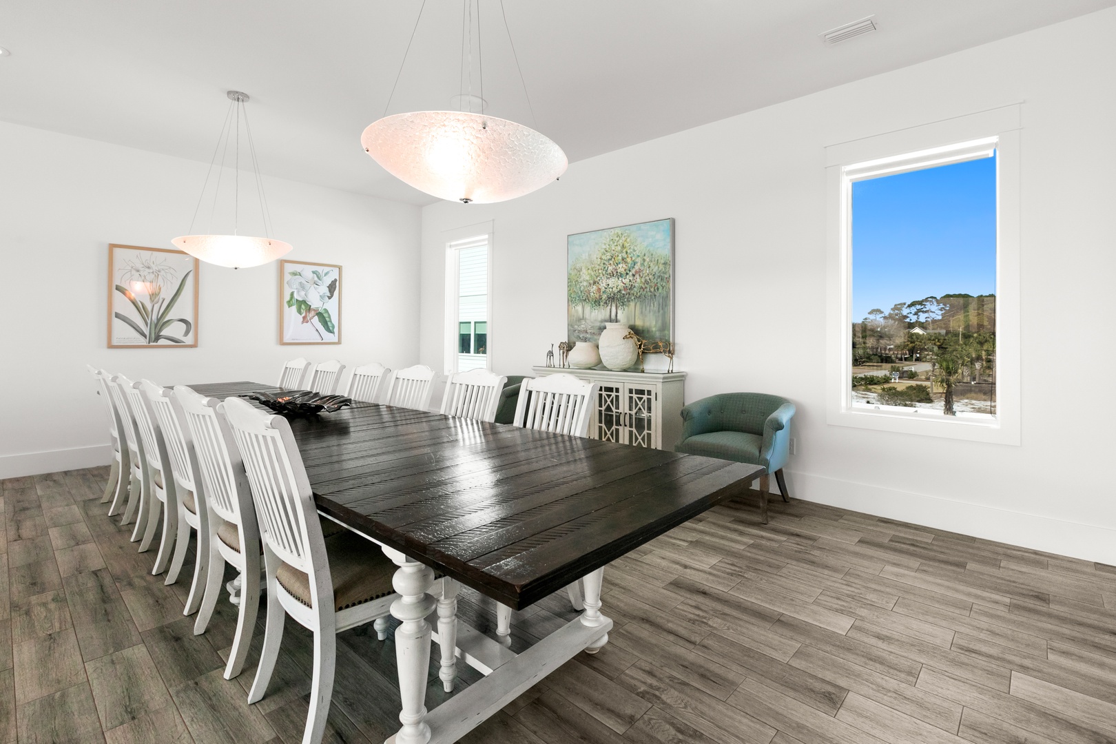 Gather everyone around this stunning farmhouse dining table under elegant pendant lighting. Natural light floods the space, while a window frames the peaceful surroundings beyond.