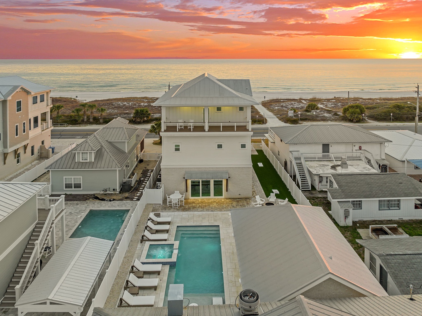 Stunning beachfront vacation home showcases pristine pools and spacious decks against a breathtaking sunset backdrop near the shore.