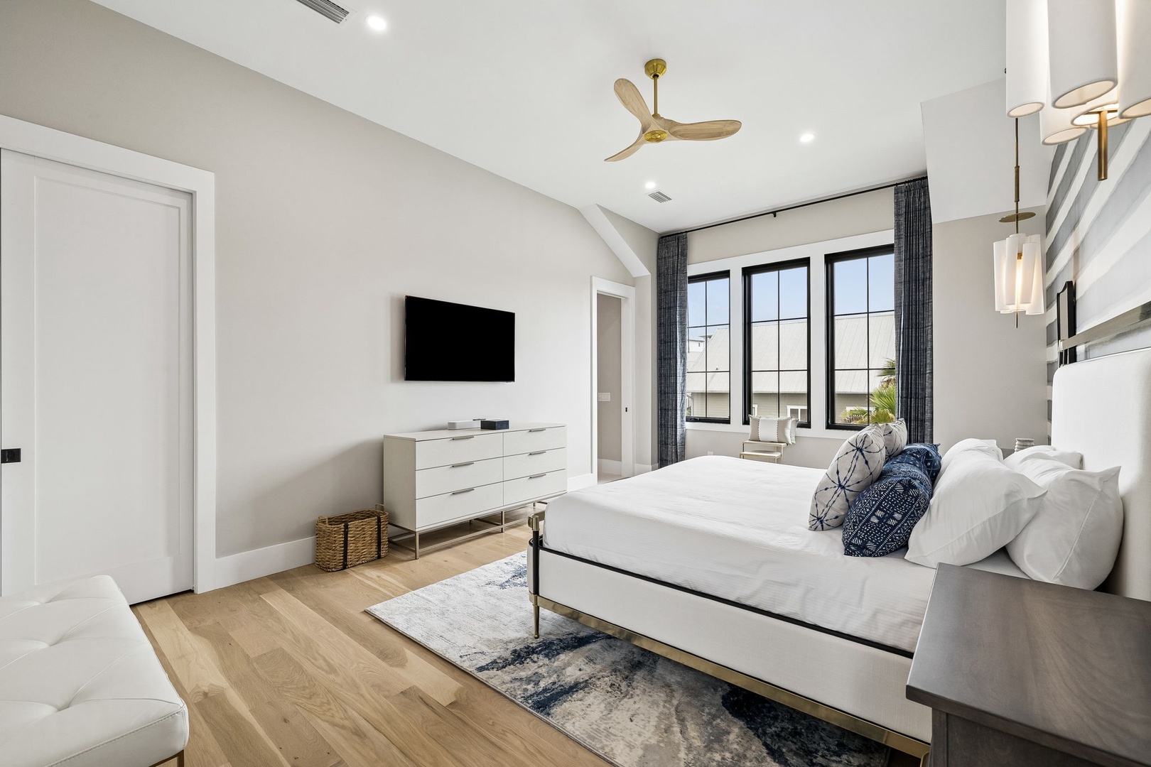 Sink into crisp linens in your bright, modern bedroom with soaring vaulted ceilings, a gentle ceiling fan, and serene natural light streaming through tall windows.