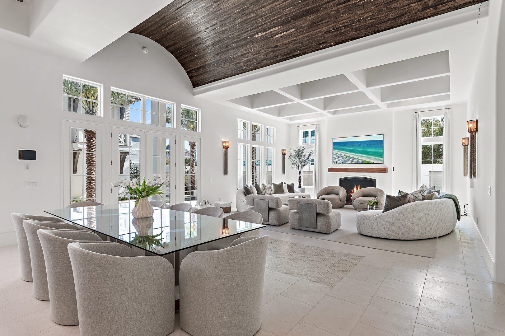 Step into your bright, open-plan sanctuary where vaulted wood ceilings and floor-to-ceiling windows frame the paradise beyond. Sink into plush seating by the fireplace and let coastal light fill your days.