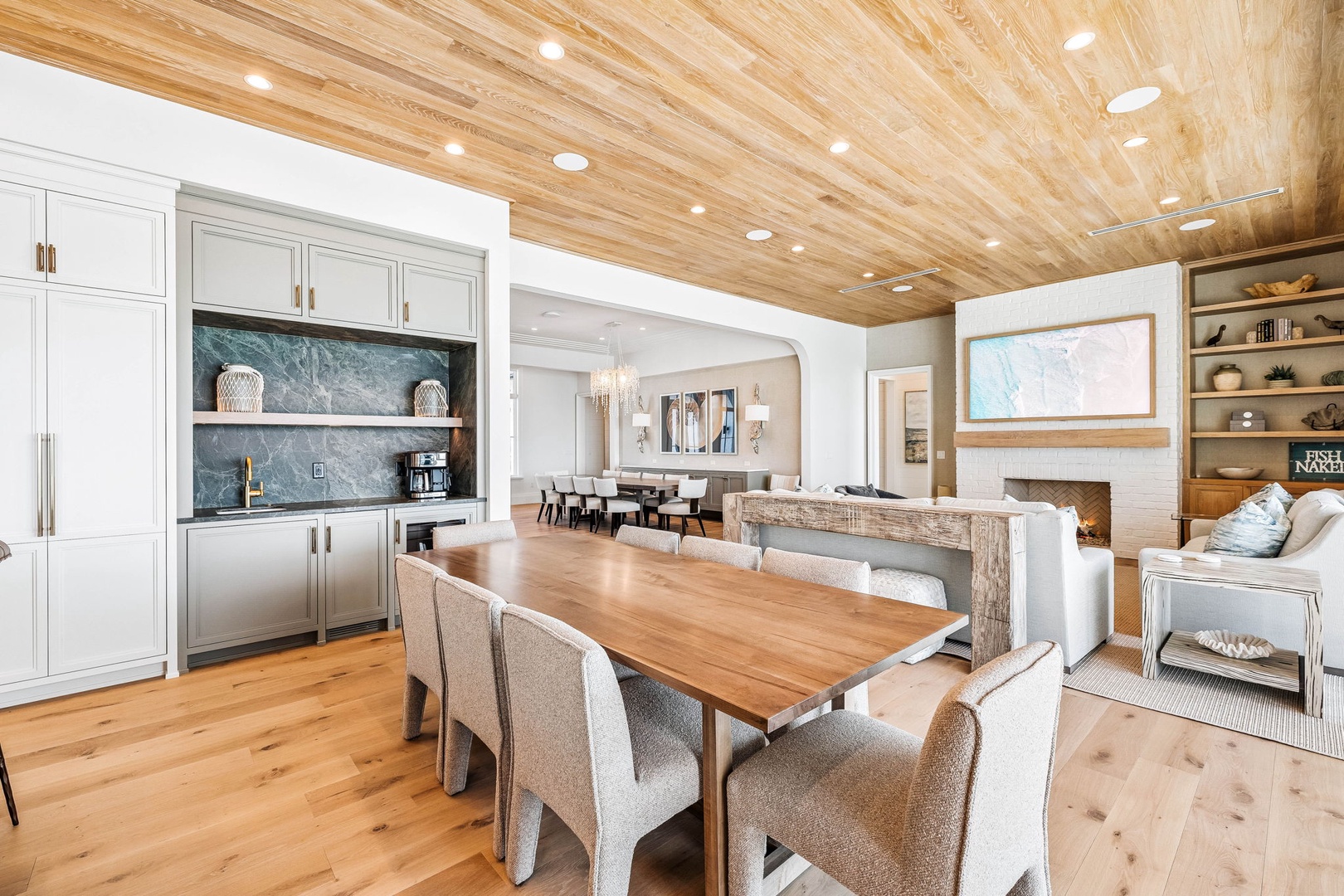 Gather around the natural wood dining table beneath soaring wood-planked ceilings, where built-in cabinetry and open shelving create a seamless flow into your living and dining spaces.