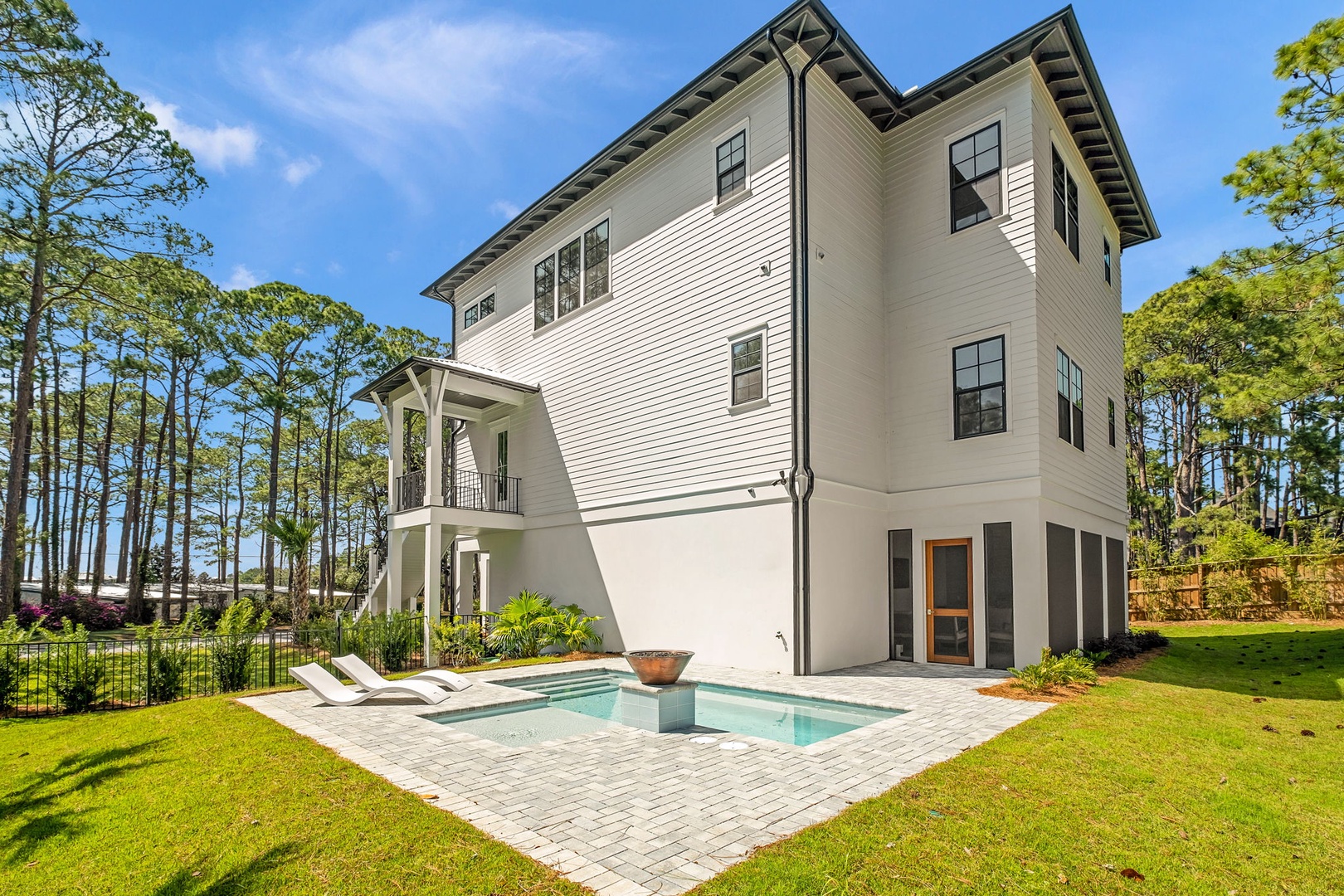 Modern three-story vacation home featuring private pool and landscaped grounds surrounded by towering pine trees.