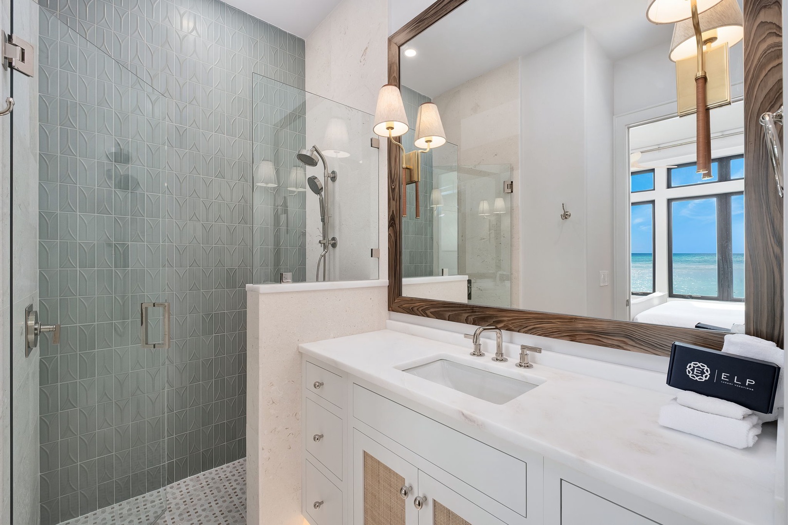 Luxuriate in your spa-like bathroom featuring elegant tiled shower, marble vanity, and serene ocean views through the window.