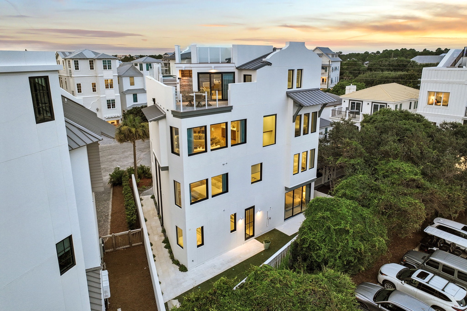 Modern coastal architecture nestled in a serene neighborhood, bathed in the warm glow of golden hour light, with lush greenery surrounding the elegant white exterior.