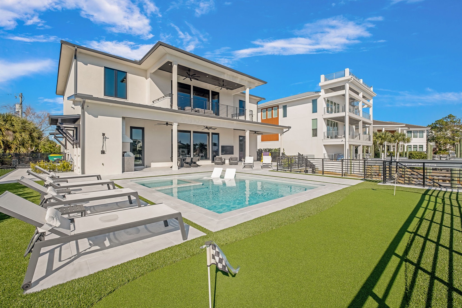 Modern waterfront vacation home featuring a private pool, spacious deck with lounge chairs, and contemporary architecture in a desirable coastal neighborhood.