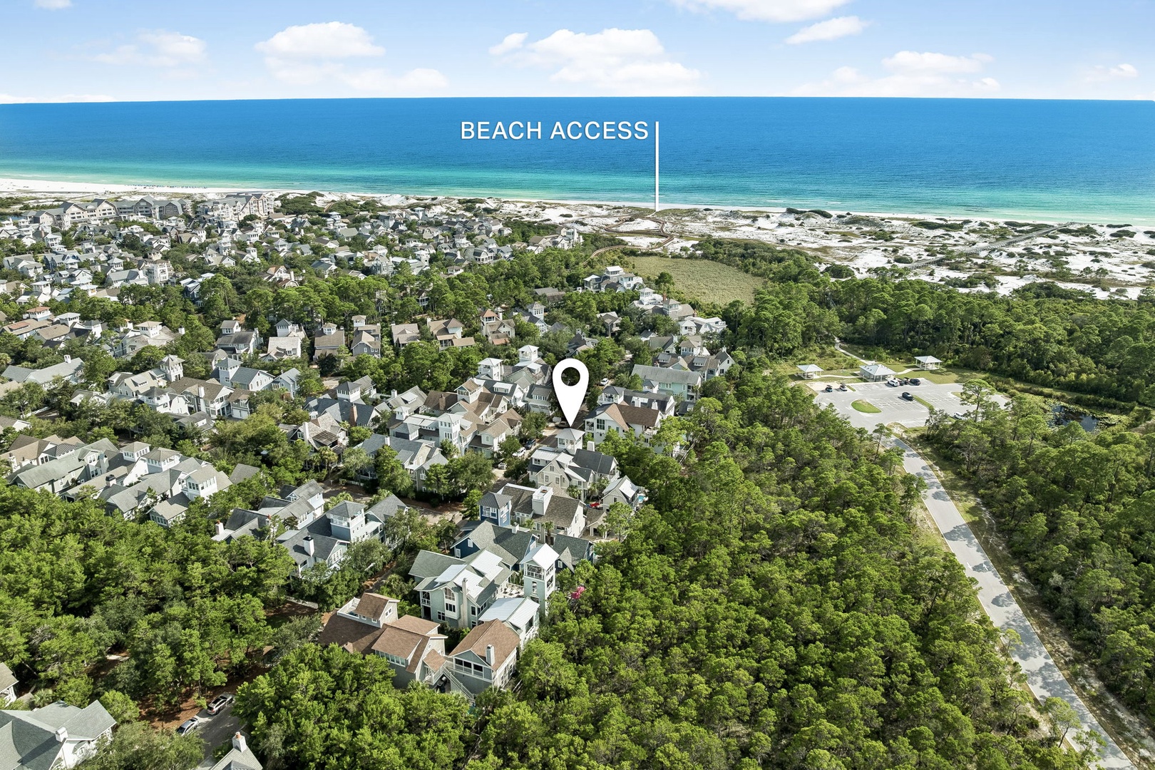 An aerial view reveals a coastal neighborhood nestled between lush greenery and pristine sandy shores, with the marked property located a short stroll from beach access.