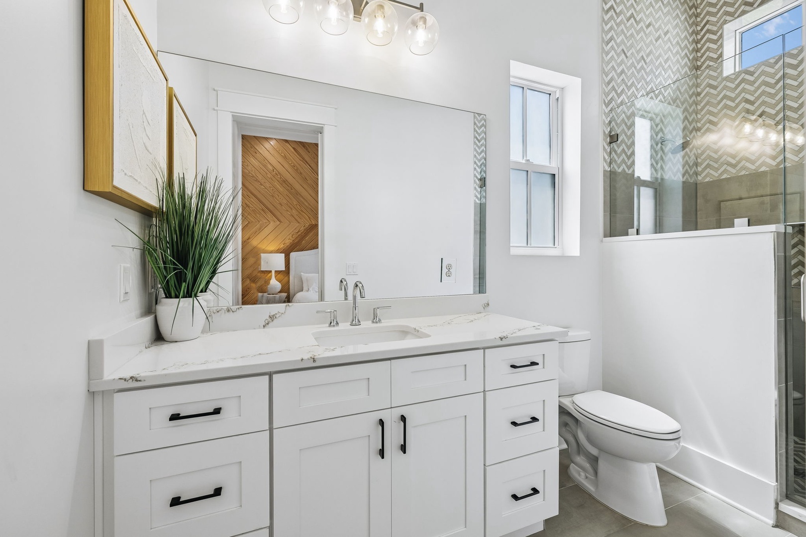 Step into your stylish sanctuary with gleaming marble counters, crisp white cabinetry, and a contemporary walk-in shower with chic chevron tile. Fresh greenery and elegant lighting complete your refreshing retreat.