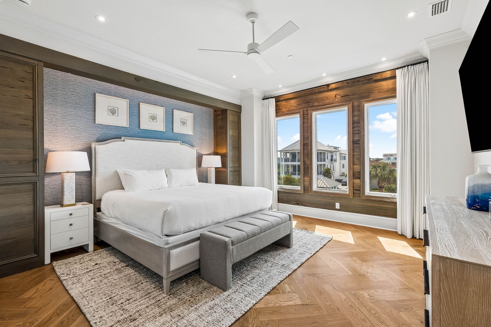 Sink into crisp white linens and wake up to beautiful views through the tall wooden-framed windows. Your stylish bedroom features elegant herringbone floors, soft lighting, and coastal-inspired decor that invites peaceful nights and refreshed mornings.