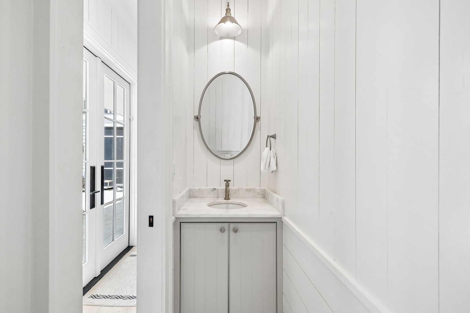 Freshen up in your bright, pristine bathroom featuring a marble-topped vanity, elegant oval mirror, and soft pendant lighting that creates a welcoming, spa-like retreat.