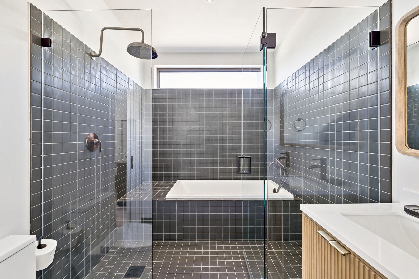 Unwind in your spa-like bathroom with rainfall shower and soaking tub, surrounded by elegant grey tiles and natural light.