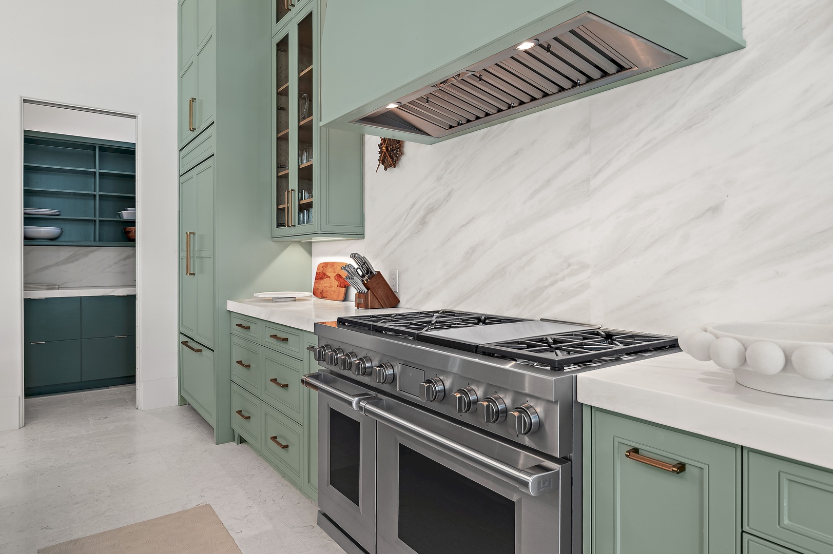 Picture yourself cooking in this elegant kitchen with sage-green cabinetry, a professional-grade gas range, sleek marble backsplash, and abundant storage—everything you need for memorable meals during your stay.